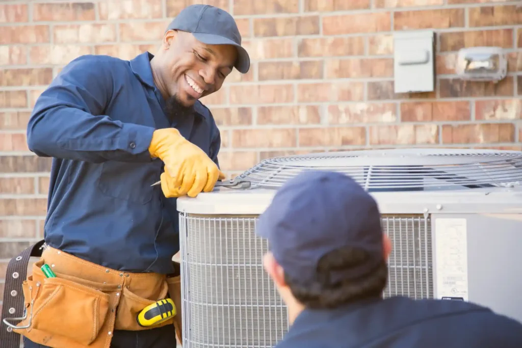 ac repairman hvac technicians in blue uniforms servicing an outdoor air conditioning unit near a brick wall with electrical meter and conduit