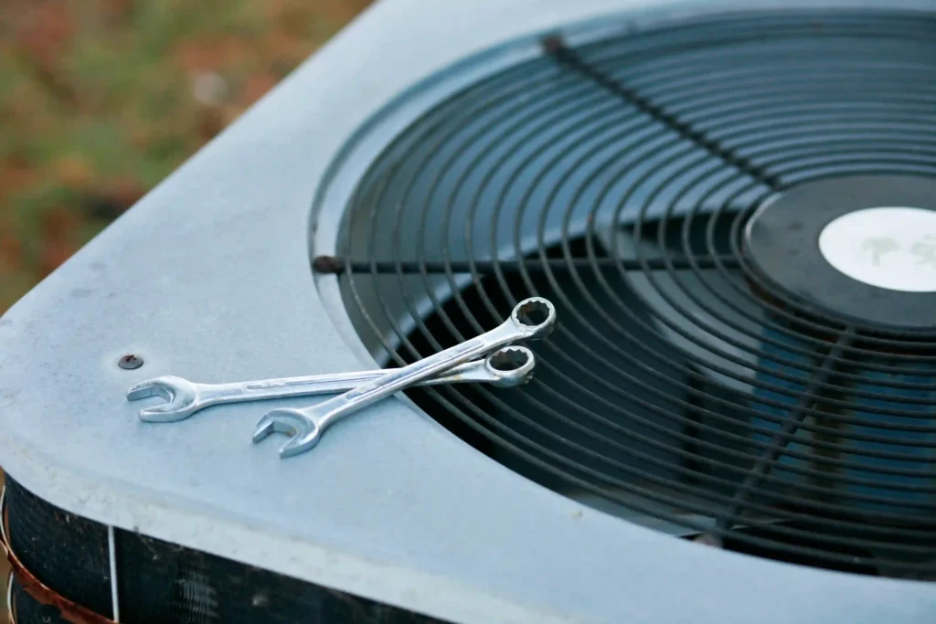 ac repairs two wrenches resting on the fan grille of an outdoor air conditioning unit, symbolizing hvac repair and maintenance tools