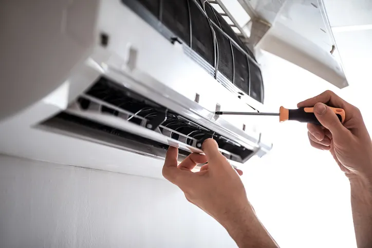 technician using a screwdriver to service a wall-mounted air conditioning unit, performing maintenance or repair work.