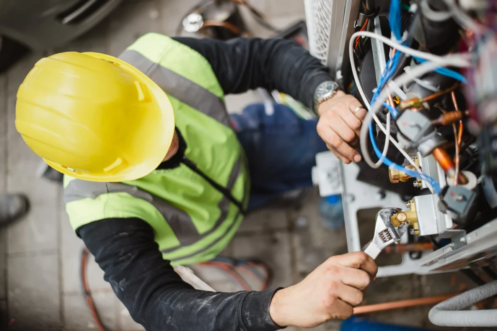 generator services worker in yellow hard hat and high-visibility vest using a wrench to service machinery with exposed wires and components
