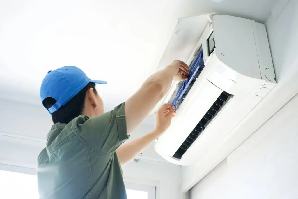 ac repair a person wearing a blue cap and a green shirt is shown cleaning or replacing the blue air filters of a white wall-mounted air conditioning unit.